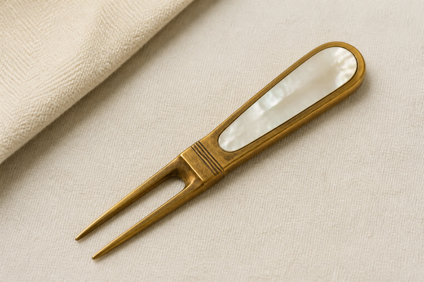 An aged brass divot tool with a mother-of-pearl inlay in the handle.