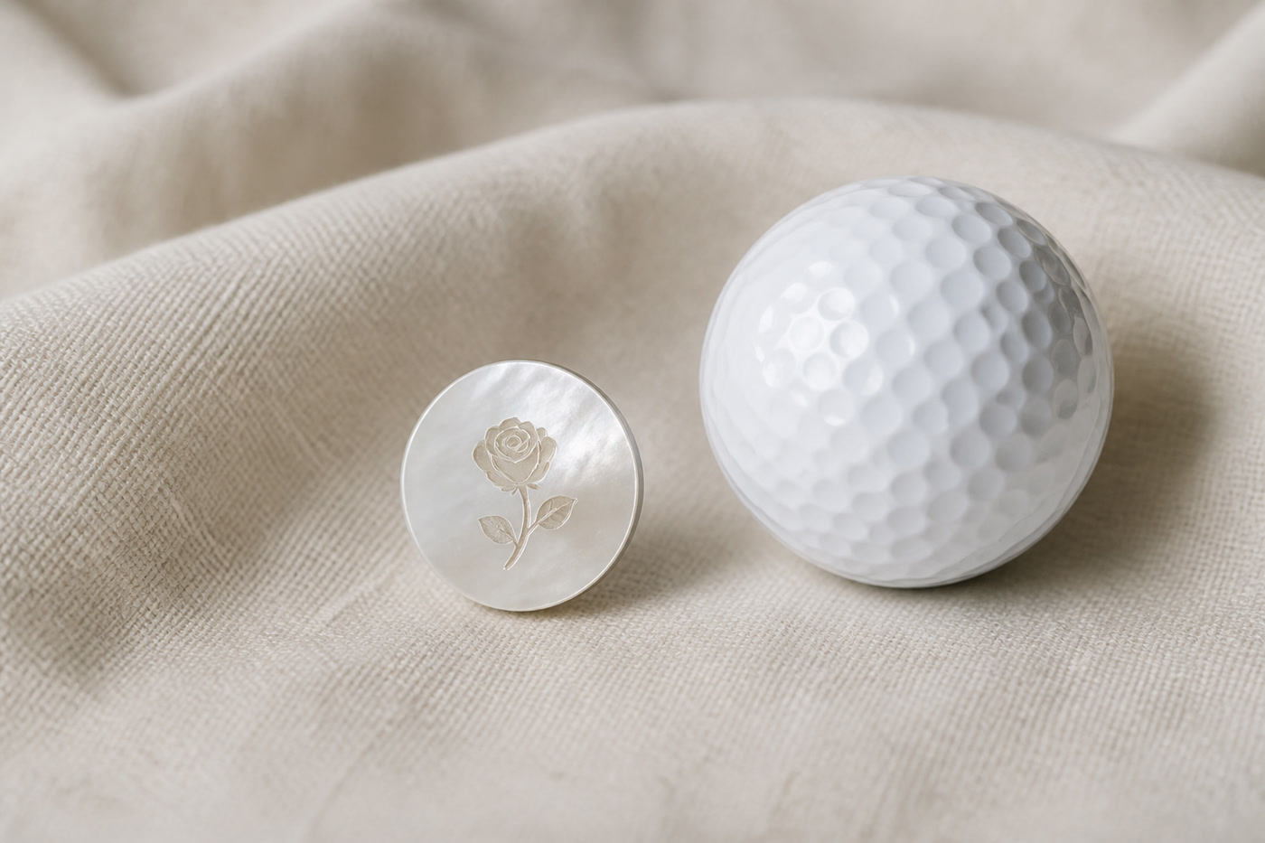 A mother-of-pearl golf ball marker engraved with a rose, beside a white golf ball.