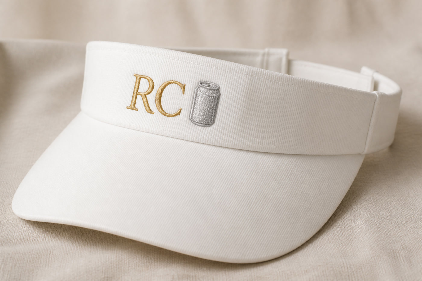 A white visor with gold RC and a small embroidered can beside the letters on the front band.