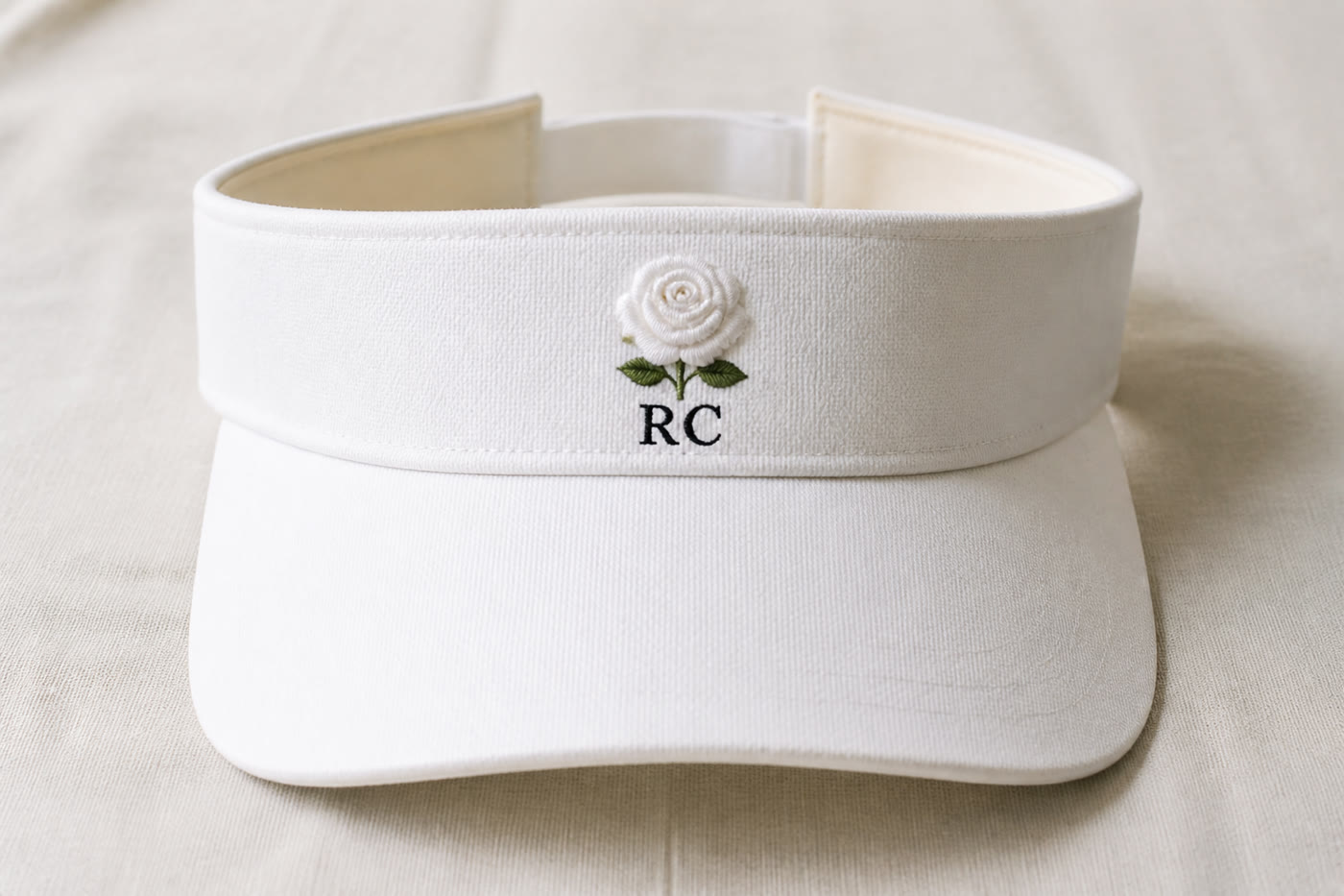 A white visor with a centered white rose and the letters RC in black beneath it.